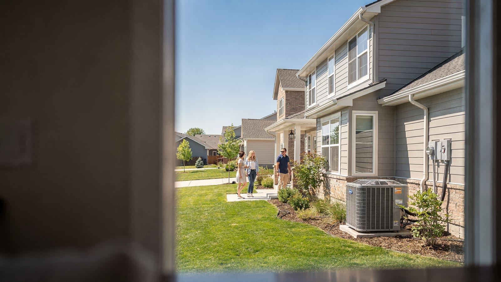 A Front Range family walking up to their Parker home on a clear summer day, AC condenser beside the house